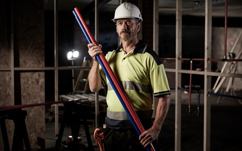 Installer on a building site holding a bunch of Sharkbite pipes.