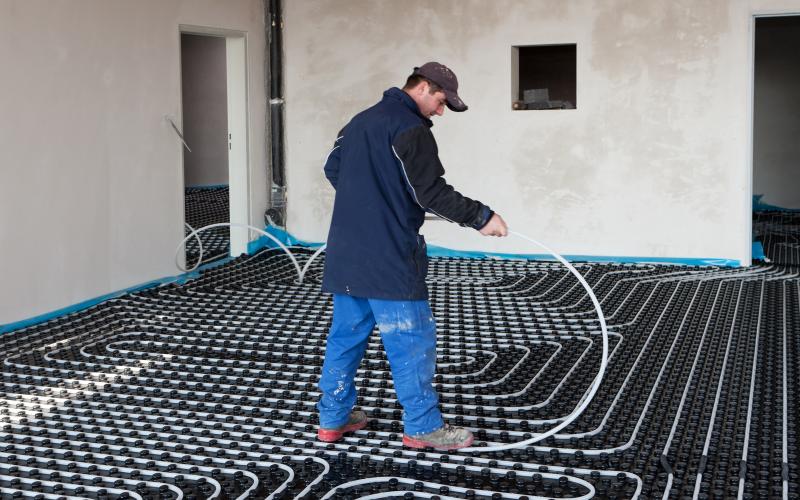 Man in blue jacket installing UFH using JG Speedfit tiles and white layflat pex pipe.