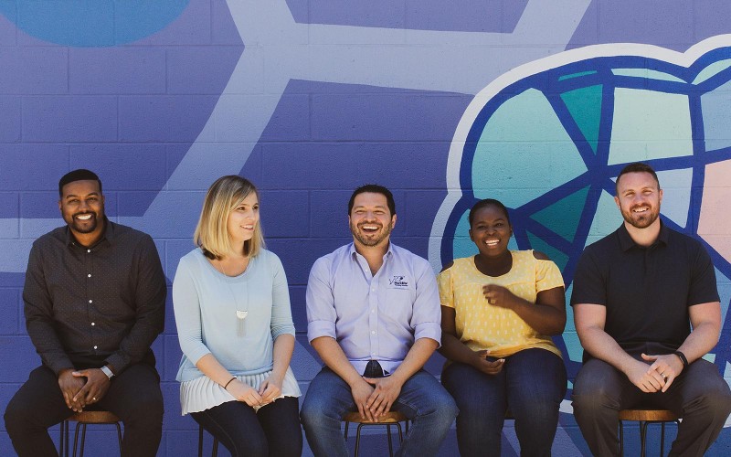 5 team members sat down behind mural wall 