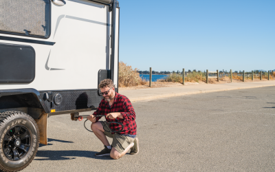 Person connecting a hose to a recreational vehicle water hookup at a campground using John Guest portable water connection system.