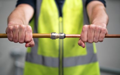 Hands joining two copper pipes with a SharkBite push-to-connect plumbing fitting during a residential plumbing installation.   