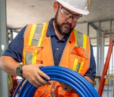 Worker installing SharkBite plumbing materials inside a new home construction project with exposed wood framing.